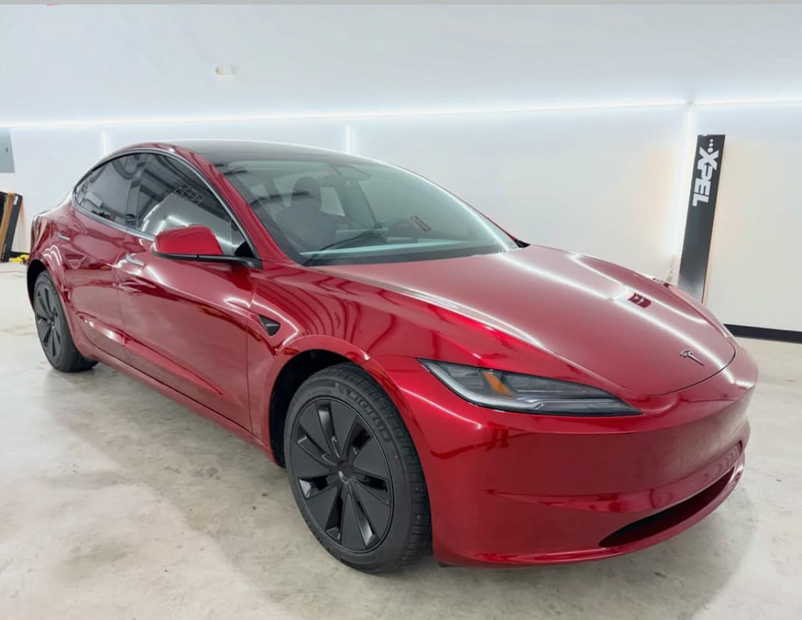 Deep red Tesla Model 3 with a protected gloss finish, photographed in a bright install bay