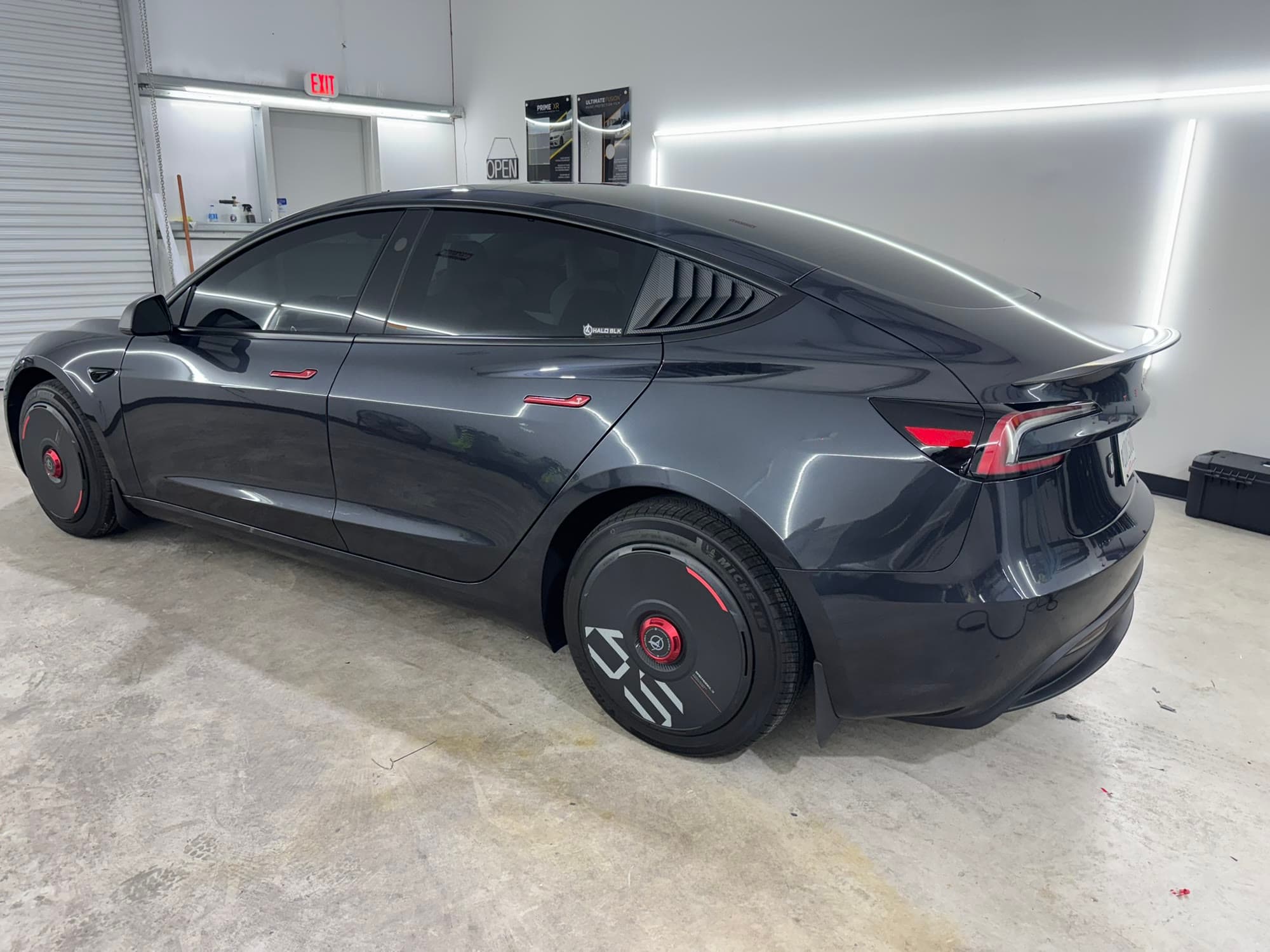 Dark gray Tesla Model 3 with fresh ceramic window tint, parked under the light bars in the TINTEC install bay